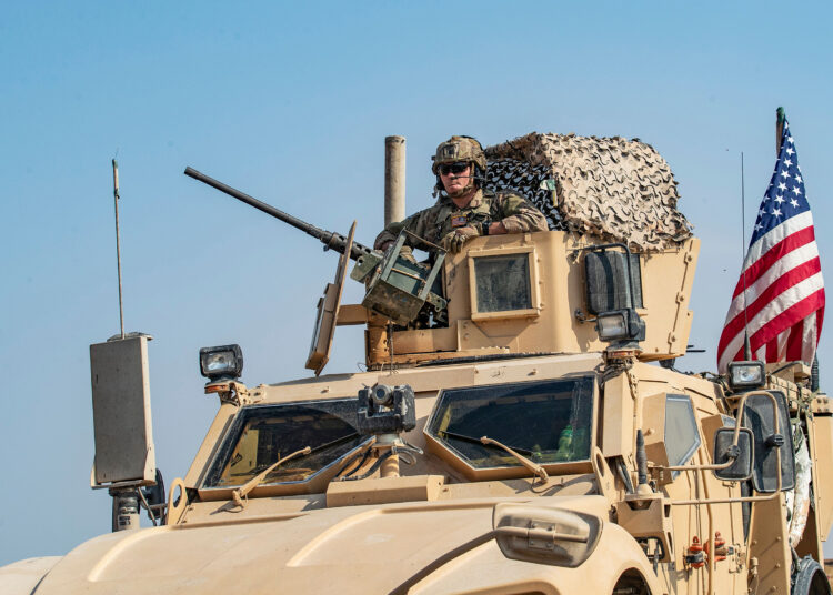 A soldier sits atop a US military vehicle, part of a convoy arriving from northern Iraq, driving through the countryside of the Syrian northeastern city of Qamishli on October 26, 2019. (Photo by Delil SOULEIMAN / AFP) (Photo by DELIL SOULEIMAN/AFP via Getty Images)